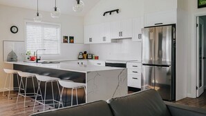 A modern kitchen with white cabinets, a stainless steel refrigerator, and a marble island with bar stools.
