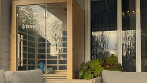 A modern outdoor seating area with wooden furniture and a glass door with a reflection of trees.