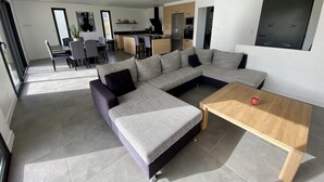A modern living room with a sectional sofa, a wooden coffee table, and a kitchen area in the background. - Single-storey house near the beach! (Cancale)