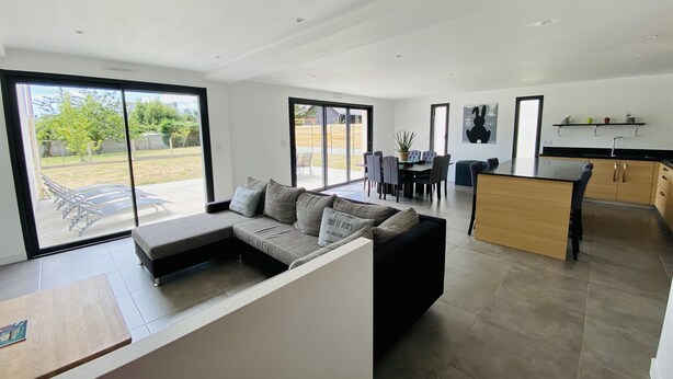 A modern living space with a dining area, kitchen, and large sliding glass doors leading to a backyard. - Single-storey house near the beach! (Cancale)