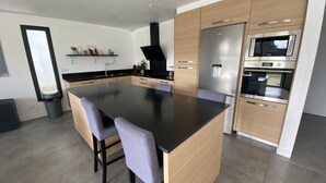 A modern kitchen with a central island, wooden cabinets, and stainless steel appliances. - Single-storey house near the beach! (Cancale)