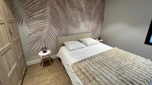 A bedroom with a bed, a nightstand, a wall with a leaf pattern, and a wooden wardrobe. - Single-storey house near the beach! (Cancale)