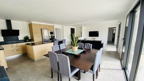 A modern kitchen with a central island, dining area with a table and chairs, and a living area with a sofa and TV. - Single-storey house near the beach! (Cancale)