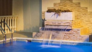 Ein Swimmingpool mit Wasserfall, einer Treppe und einer Steinmauer.