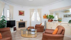 Ein modernes Wohnzimmer mit einem Glastisch, braunen Ledersofas, einem Flachbildfernseher und einem Kamin.