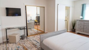 A bedroom with a bed, a desk, a TV, a wardrobe, and a mirror.