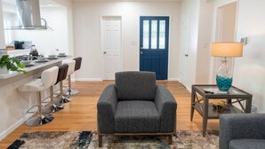 A modern living room with a grey armchair, a glass coffee table, and a blue door in the background.
