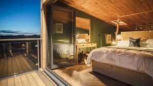 A bedroom with a large bed, a wooden ceiling, a nightstand, and a glass door leading to a balcony. - Tawny Lodge - 1 Bedroom - Blossom Farm (Haverfordwest)