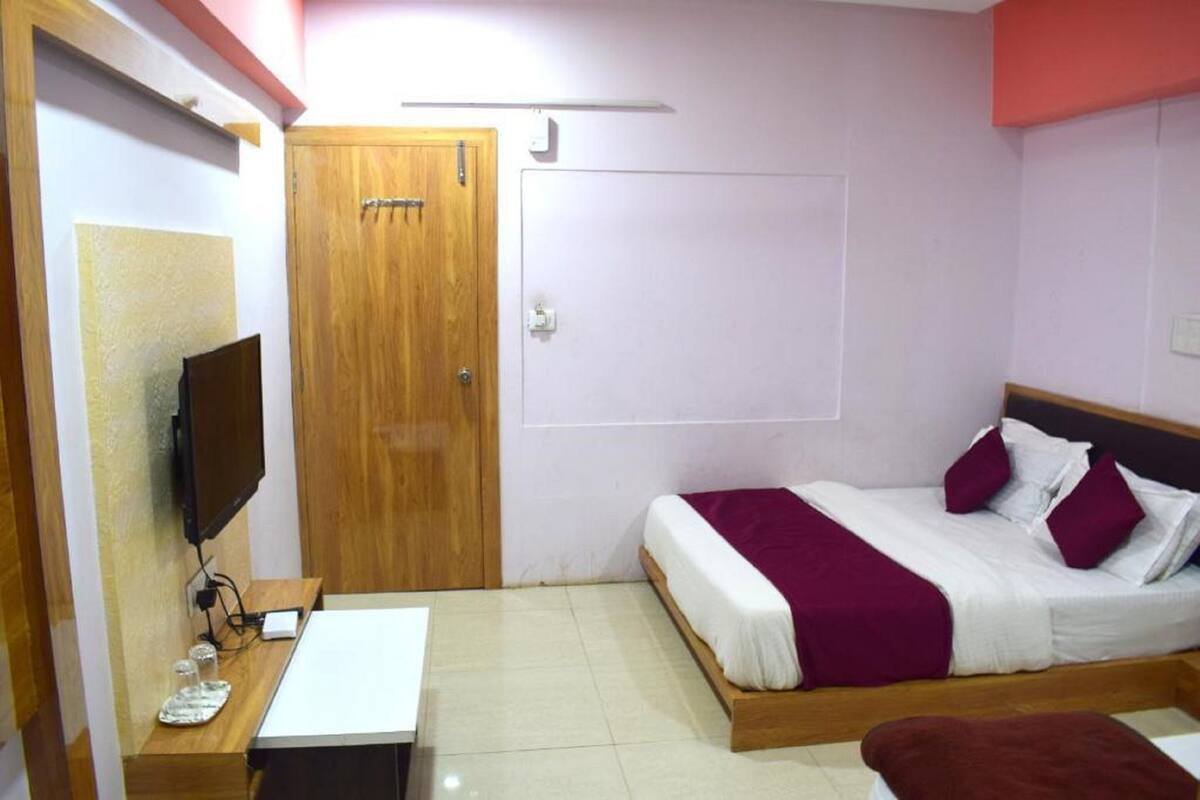 A bedroom with a bed, a desk, a television, and a door.