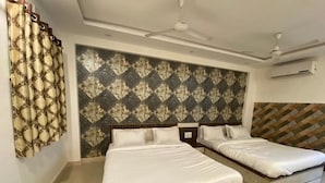 Une chambre d’hôtel avec deux lits simples, un mur décoré de motifs, un ventilateur de plafond et un appareil de climatisation.