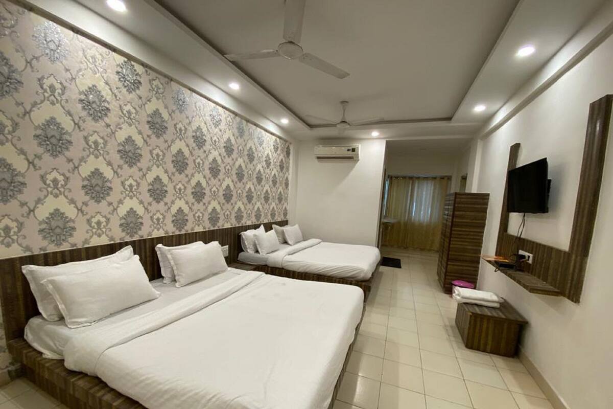 A hotel room with two beds, a TV, a ceiling fan, and patterned wallpaper.