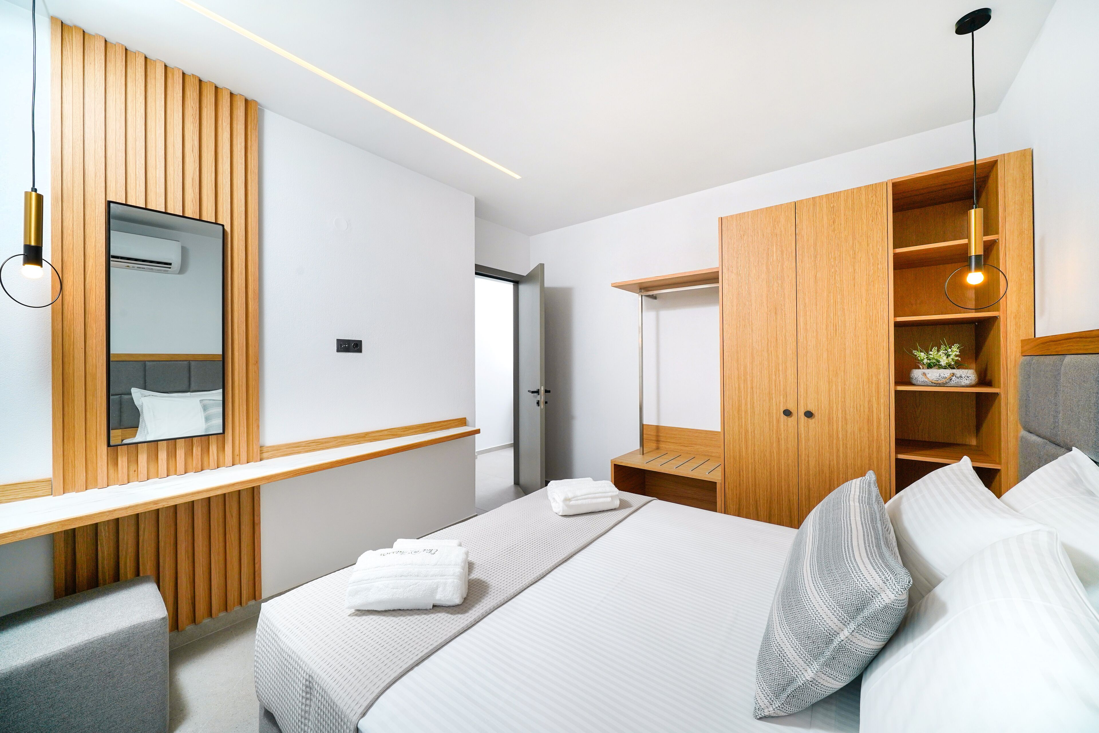 A modern hotel room with a large bed, a wooden wardrobe, a bedside table, and a mirror.