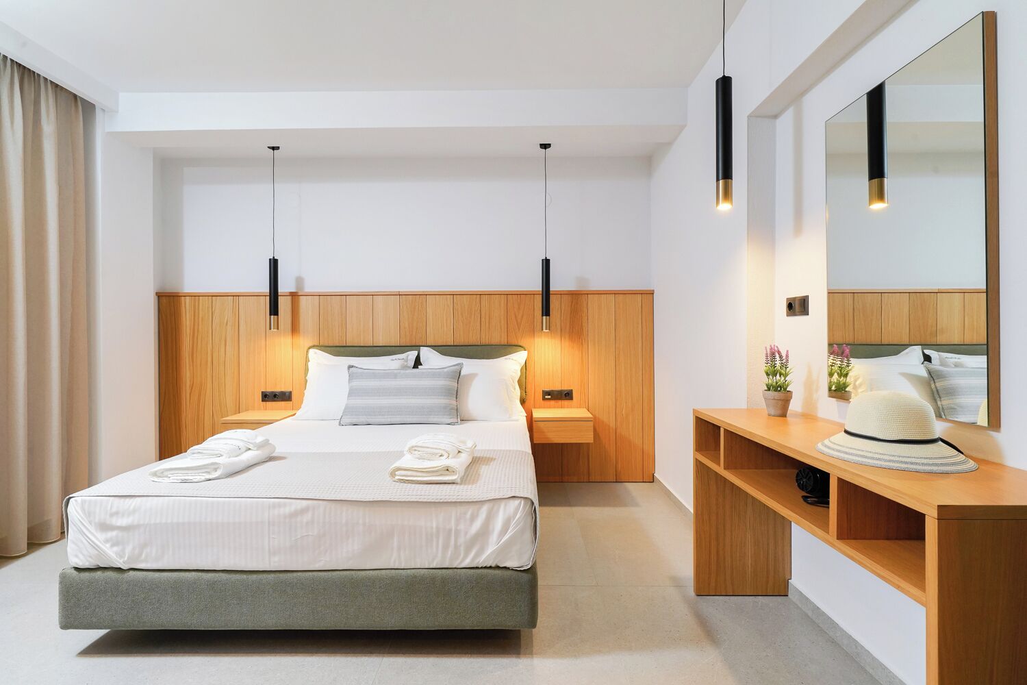 Habitación de hotel moderna con una cama grande, mesitas de noche, cabecero de madera, un espejo y un escritorio con un sombrero.