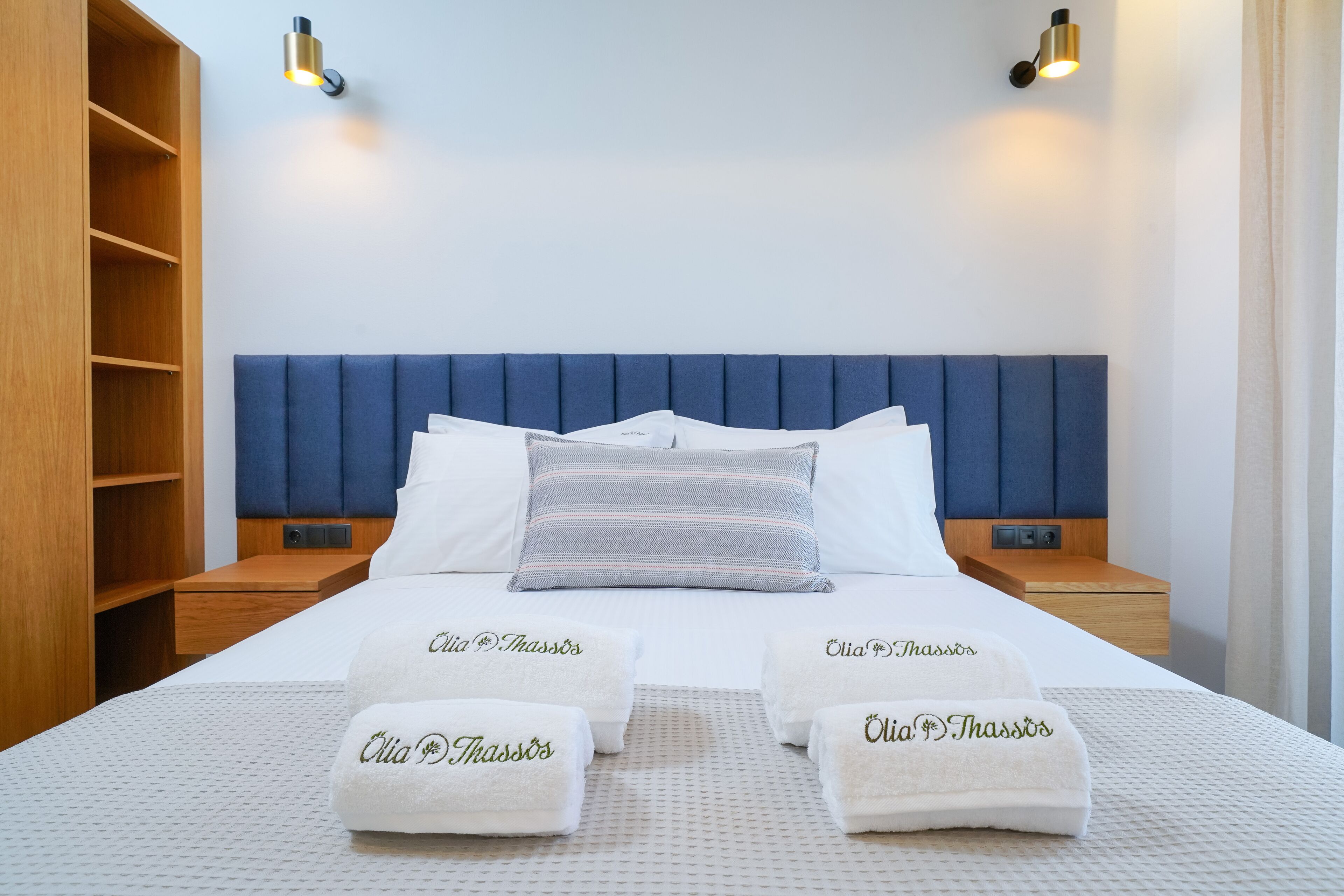 A hotel room with a large bed, a blue headboard, two bedside tables, and a wooden wardrobe.