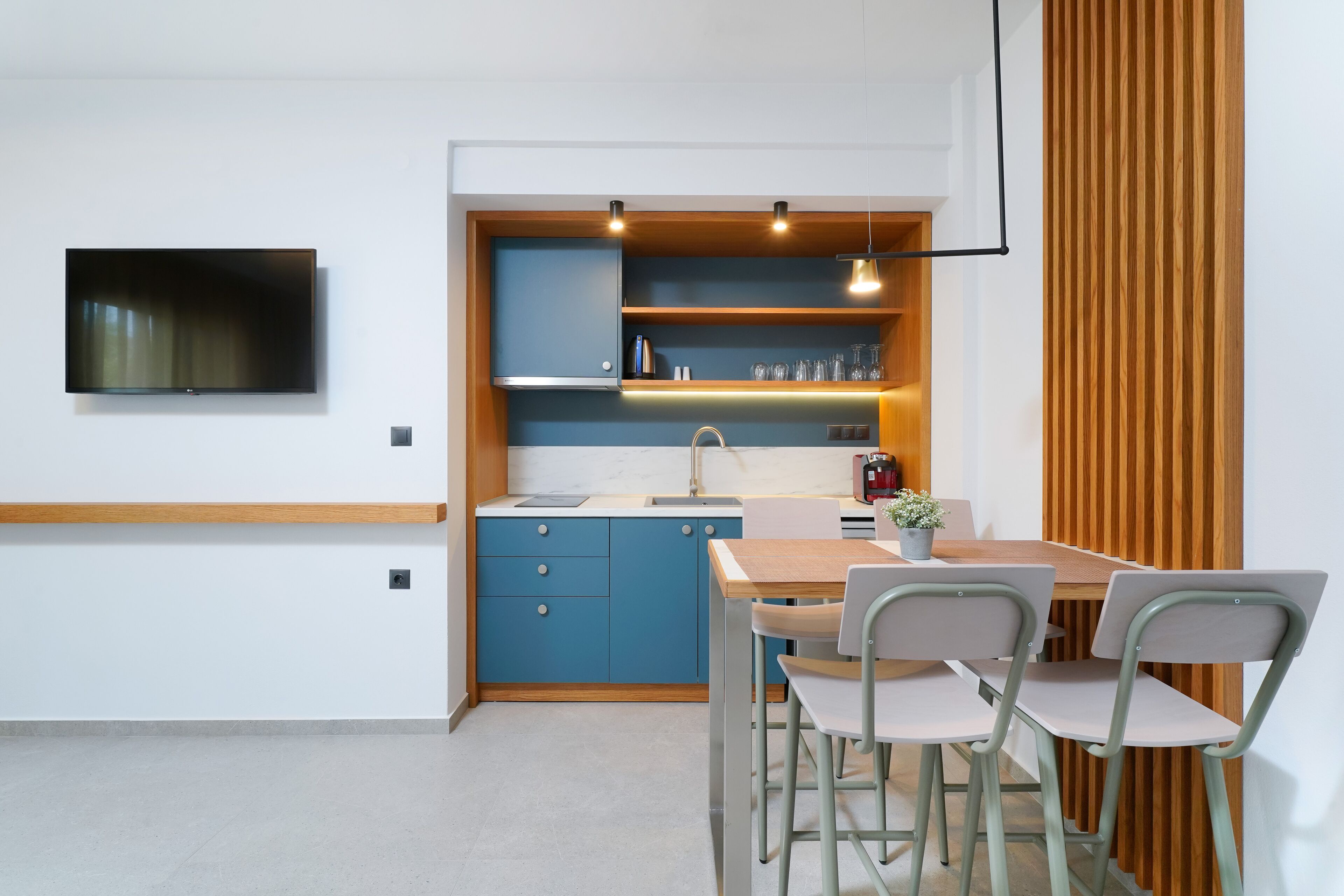 A modern kitchen with blue cabinets, a wooden countertop, and a dining area with two chairs and a table.