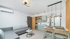 Un salon moderne avec un canapé gris, une petite table ronde agrémentée d’une plante, et un coin repas avec une table et des chaises en osier.