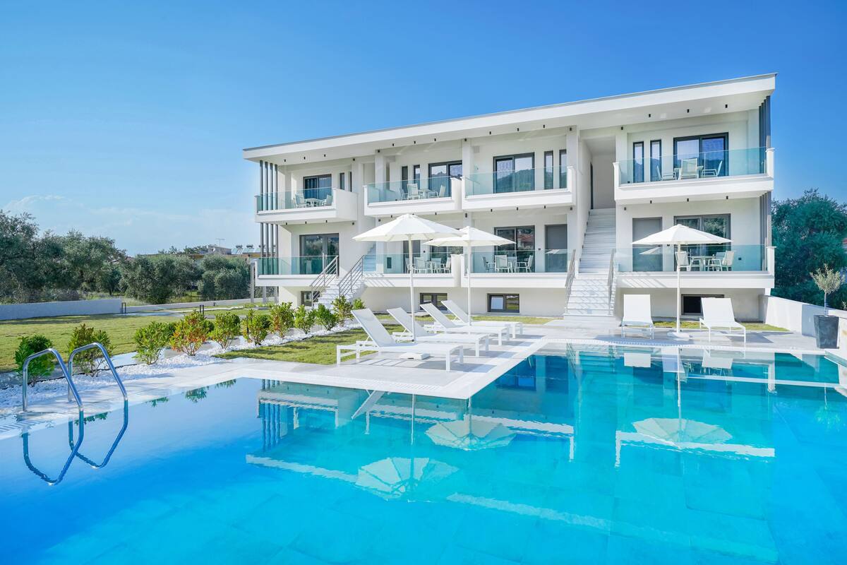 A modern two-story building with a swimming pool, outdoor seating, and a clear view of the surrounding landscape.
