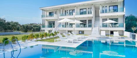 A modern two-story building with a swimming pool, outdoor seating, and a clear view of the surrounding landscape.