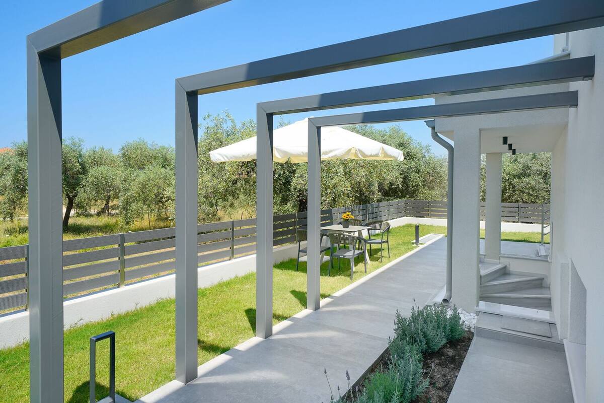 A modern outdoor patio area with a concrete pathway, a table with chairs, and a white umbrella.