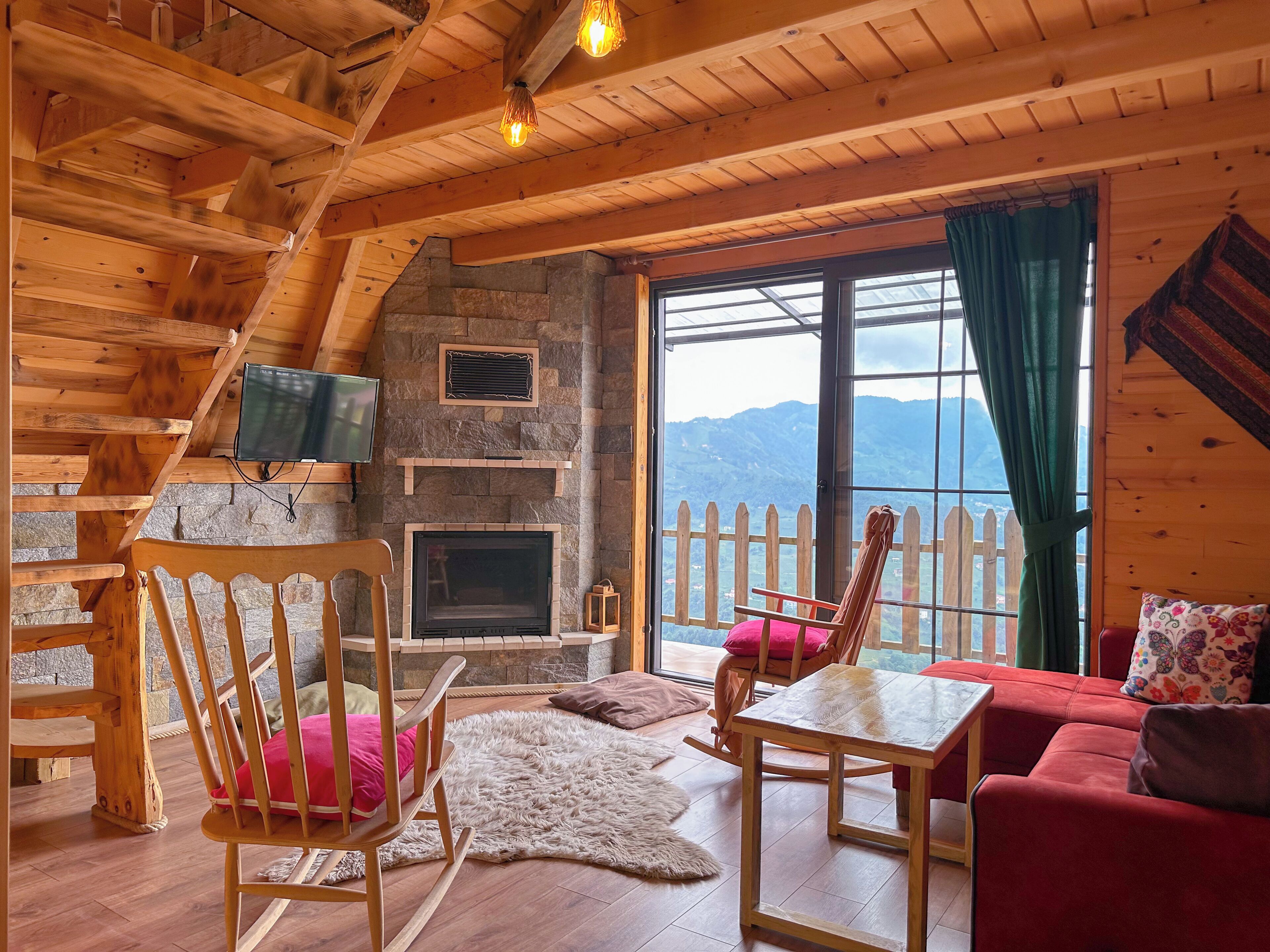 A cozy cabin interior with a stone fireplace, wooden furniture, and a scenic mountain view.