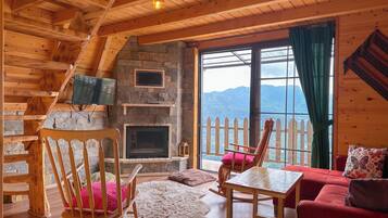 A cozy cabin interior with a stone fireplace, wooden furniture, and a scenic mountain view.