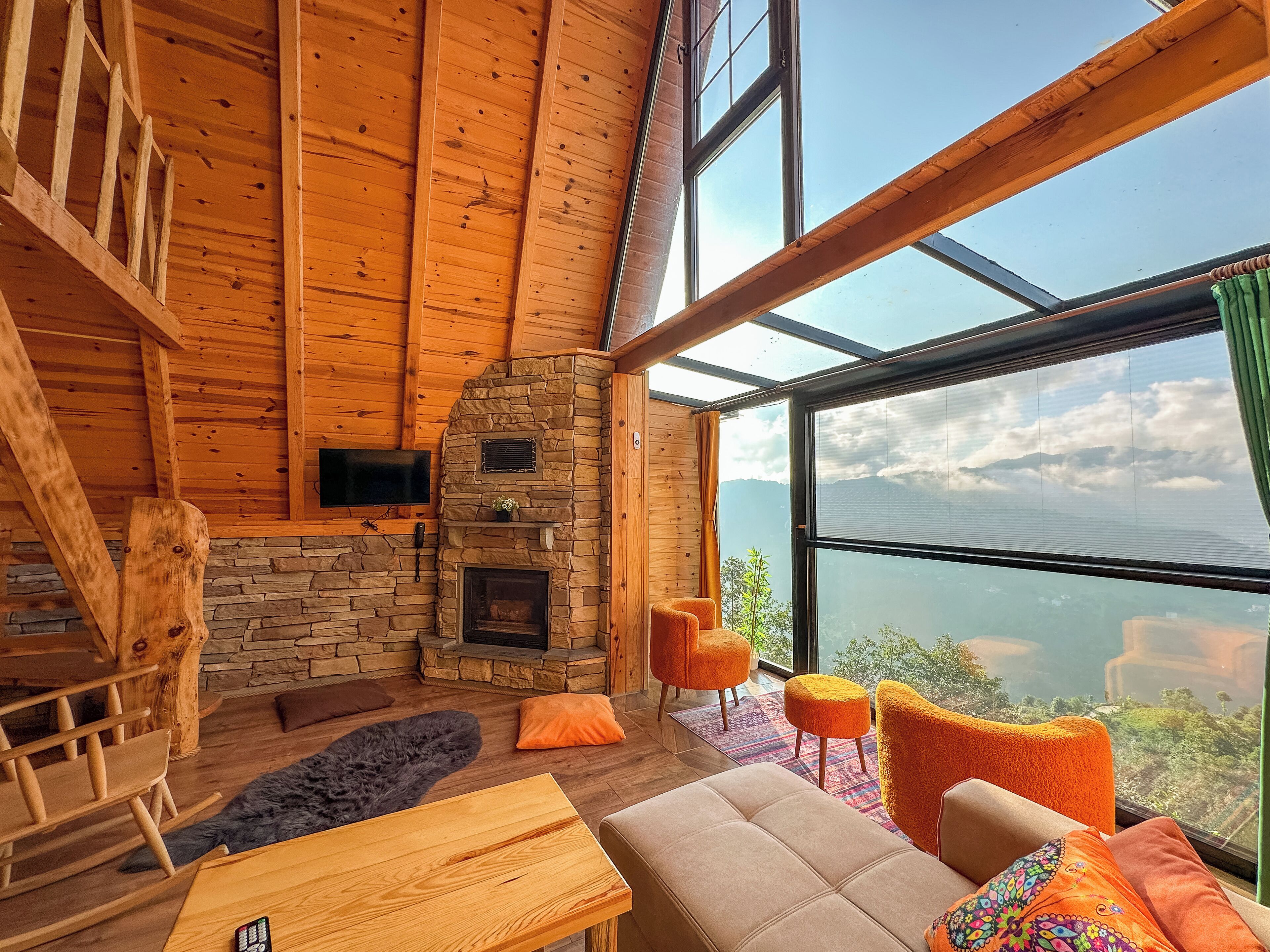 A cozy cabin interior with a stone fireplace, wooden walls, and large windows offering a mountain view.