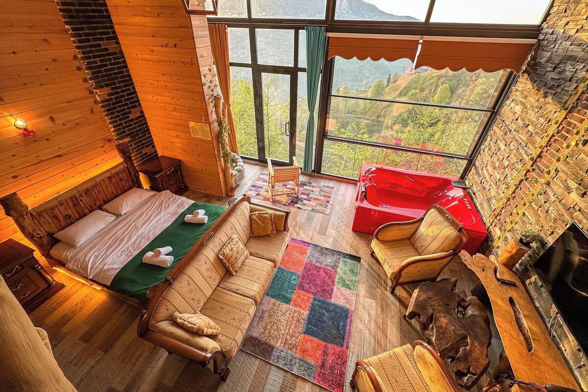 A cozy room with a bed, a sofa, a red chair, and a fireplace.