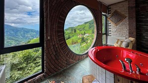 Een badkamer met een groot raam, een rood bad en uitzicht op groene heuvels.