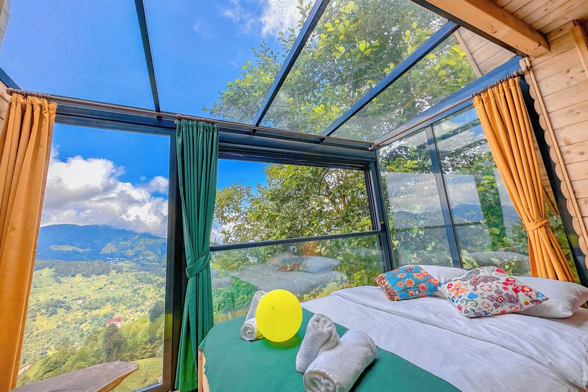 A room with a large glass window offering a scenic view of green hills and a clear sky.