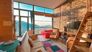 A cozy room with a large window, a wooden sofa, a red chair, a TV, and a wooden ladder.