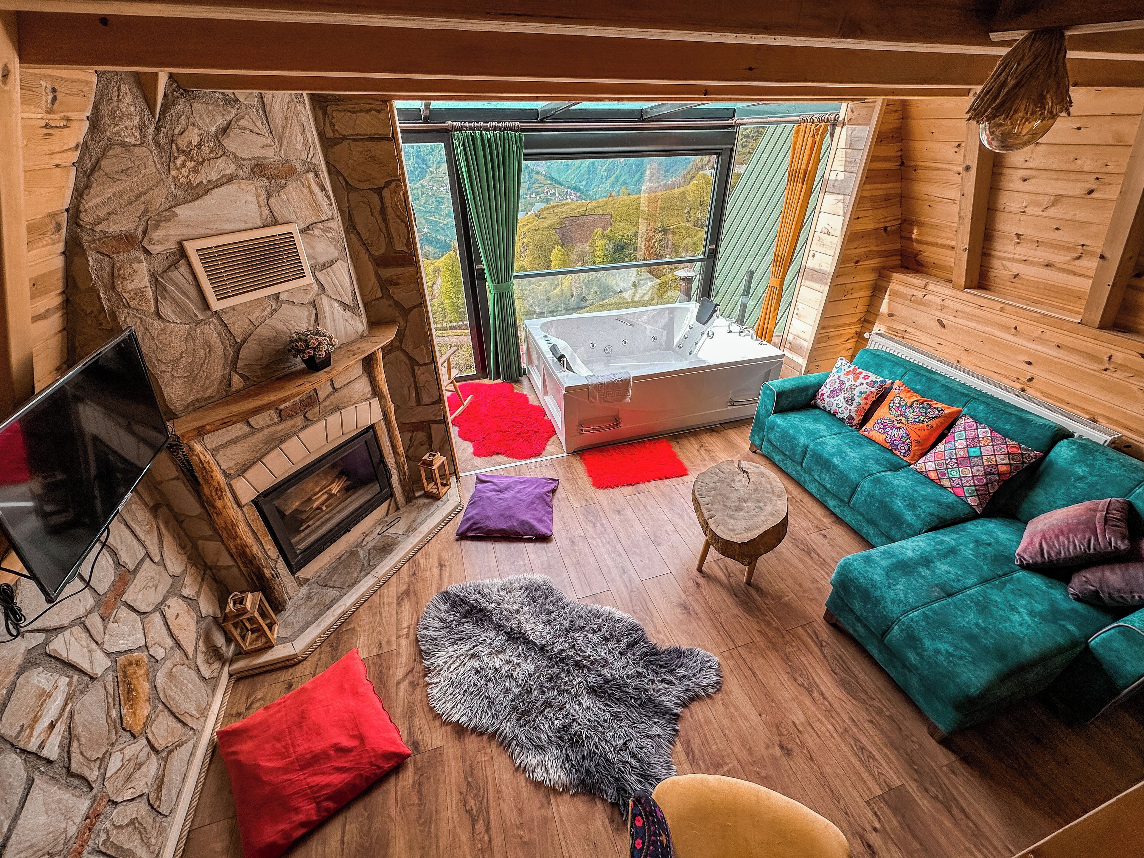 Een gezellig interieur van een chalet met een stenen open haard, een groene bank en een bubbelbad.