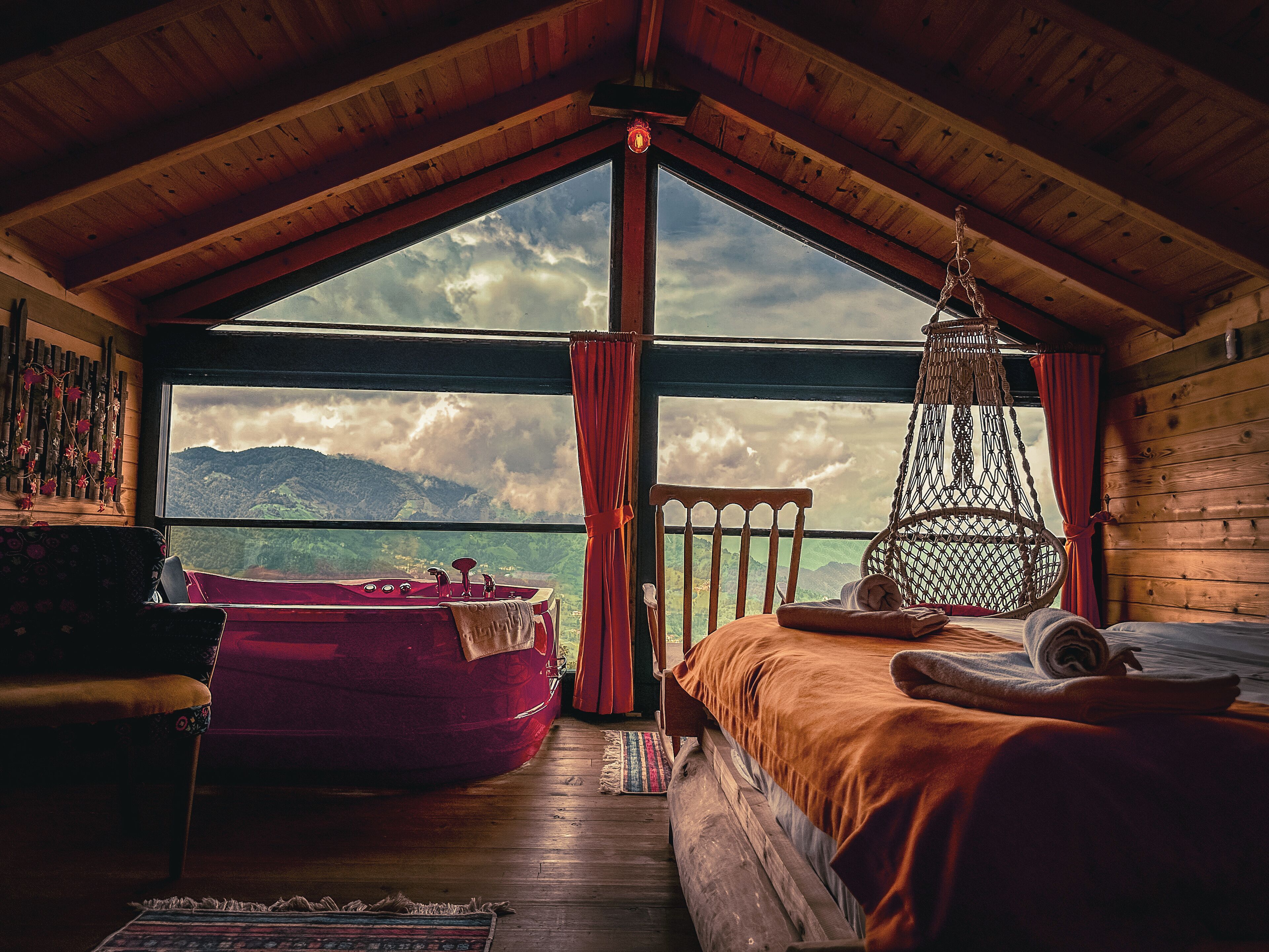 Una habitación acogedora con un ventanal grande, una cama, una silla y un sillón colgante.