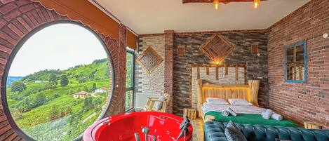 Una habitación con un ventanal circular grande, una bañera roja, un techo de madera, una cama con colcha verde y un sofá azul.