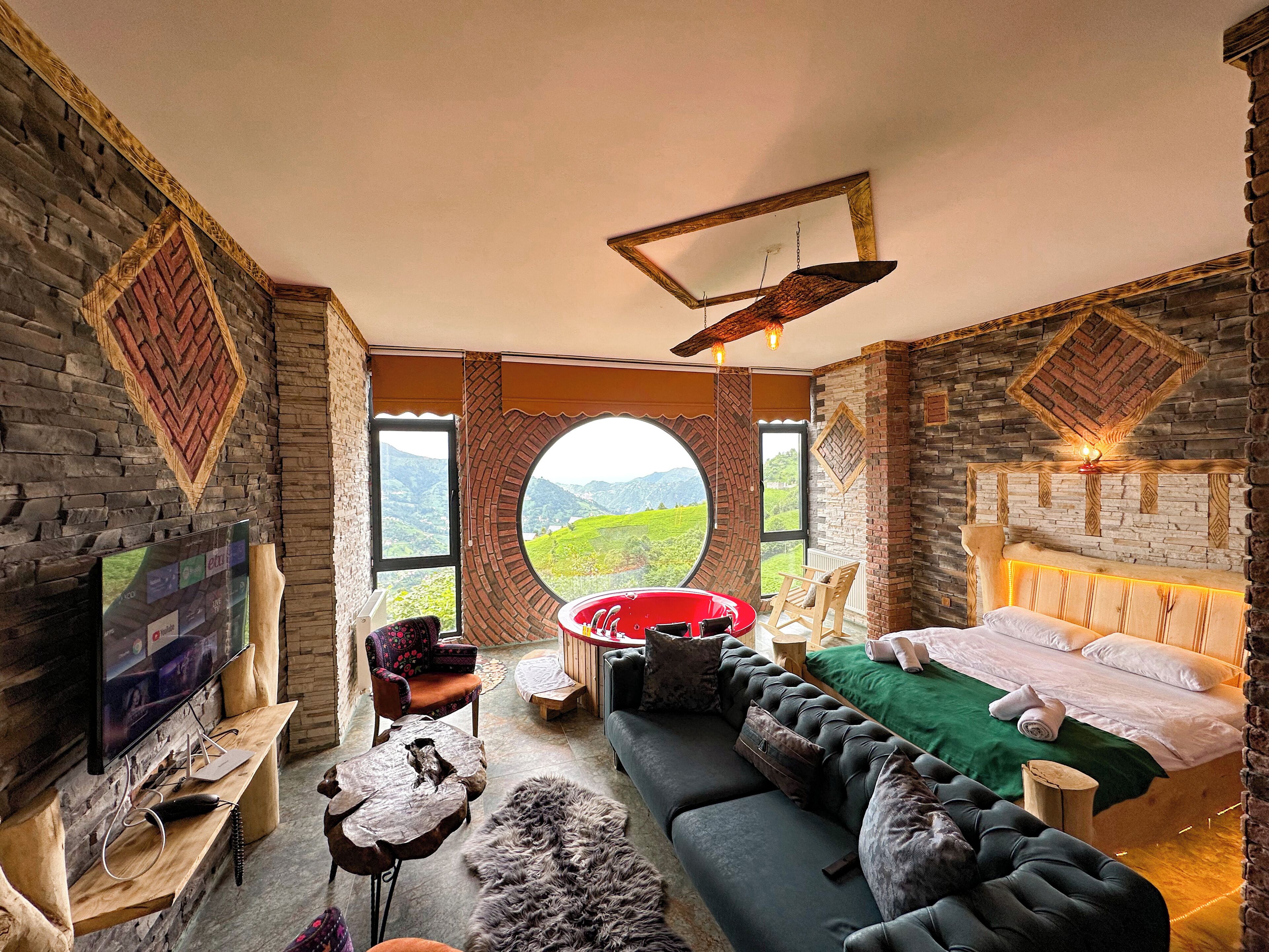 A cozy room with a large bed, a sofa, and a TV. There's a window with a view of green hills.
