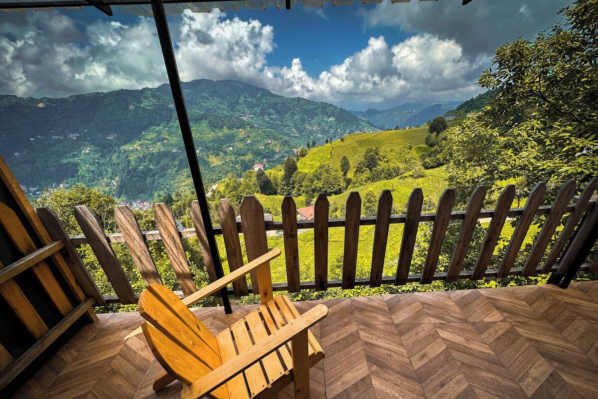 A wooden chair on a herringbone-patterned floor, overlooking a mountainous landscape with a wooden fence.