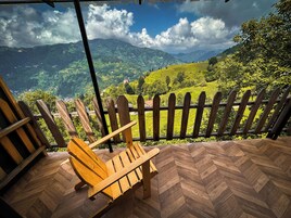 Uma cadeira de madeira sobre um piso com padrão herringbone, com vista para uma paisagem montanhosa e uma cerca de madeira.