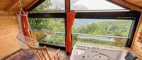 Un interior de madera con un ventanal grande, un sillón colgante y un jacuzzi.