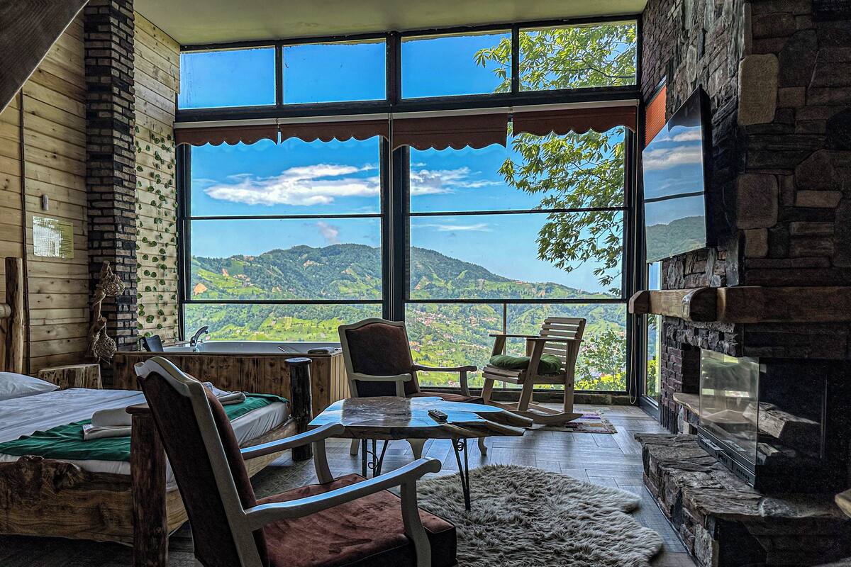 A cozy room with a large window offering a mountain view, a fireplace, and rustic wooden furniture.