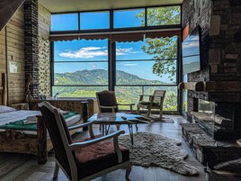 Una habitación acogedora con un amplio ventanal que ofrece vistas a la montaña, una chimenea y muebles de madera rústica.