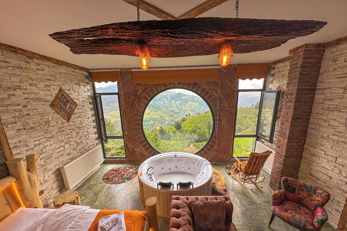 A bedroom with a large circular window, a bathtub, a bed, and a chair.