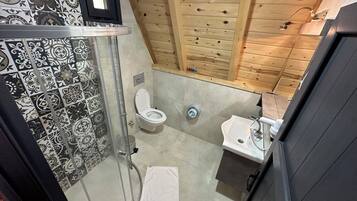 Een badkamer met douche, toilet en wastafel, met tegelwerk met een patroon en houten lambrisering.
