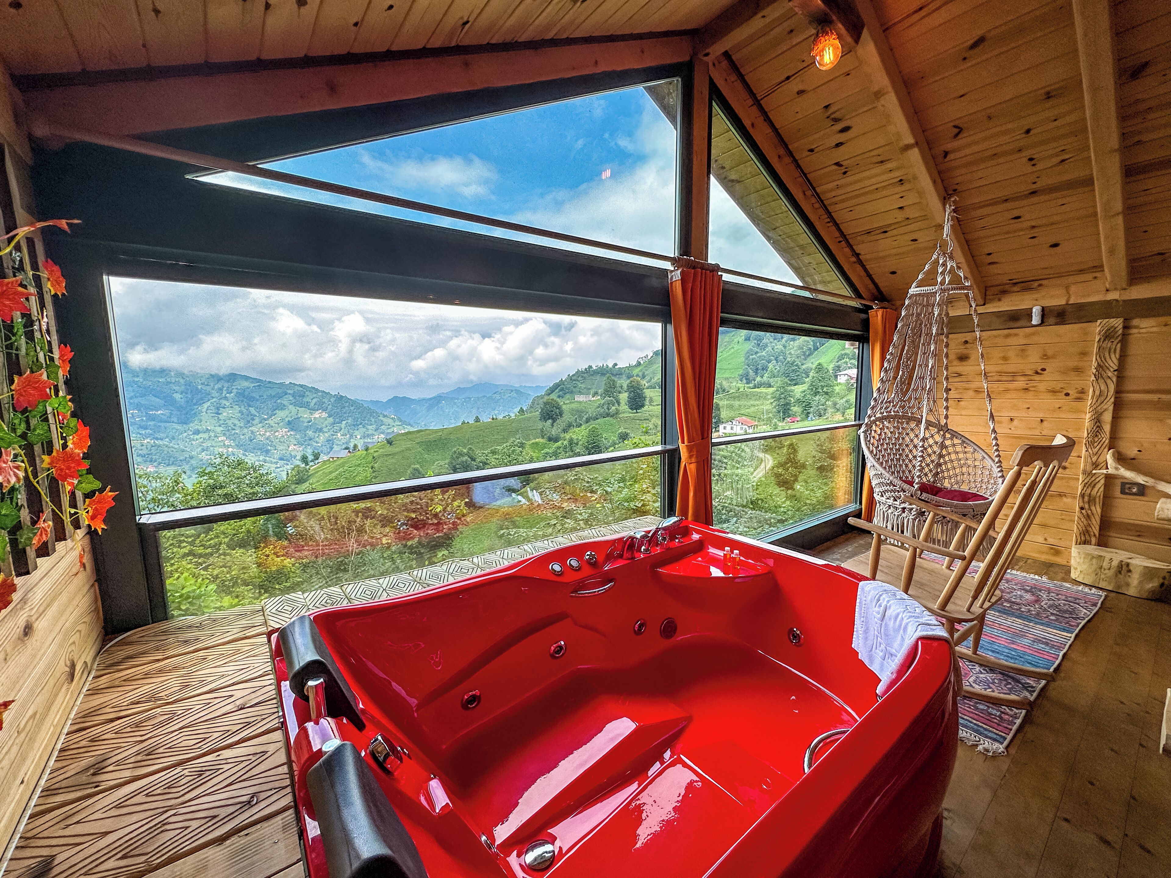 Una bañera roja en una habitación con ventanas amplias que ofrecen vistas a colinas verdes y un lago.