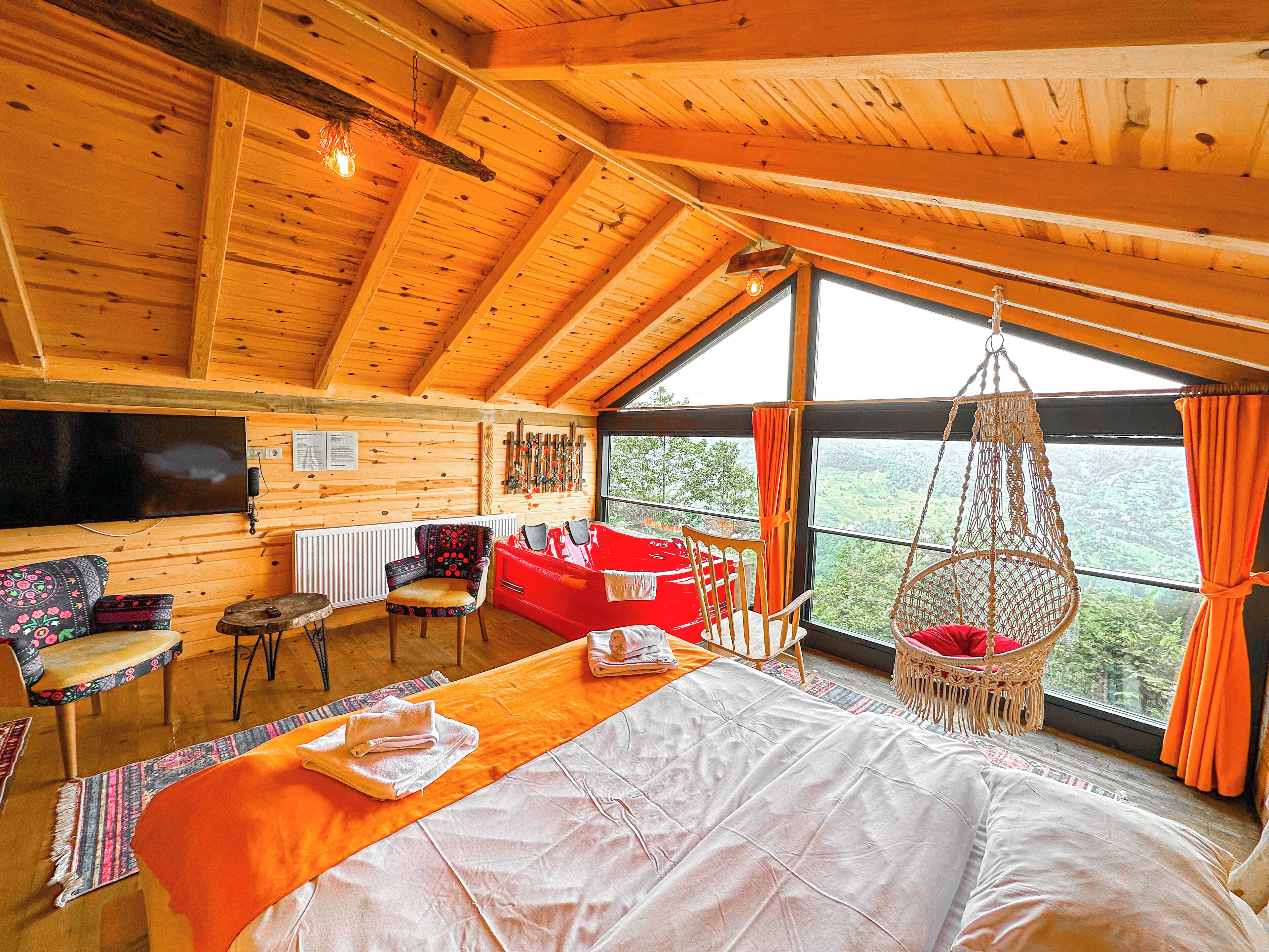 A cozy cabin interior with a large bed, a red sofa, a wooden dining table, and a television mounted on the wall.