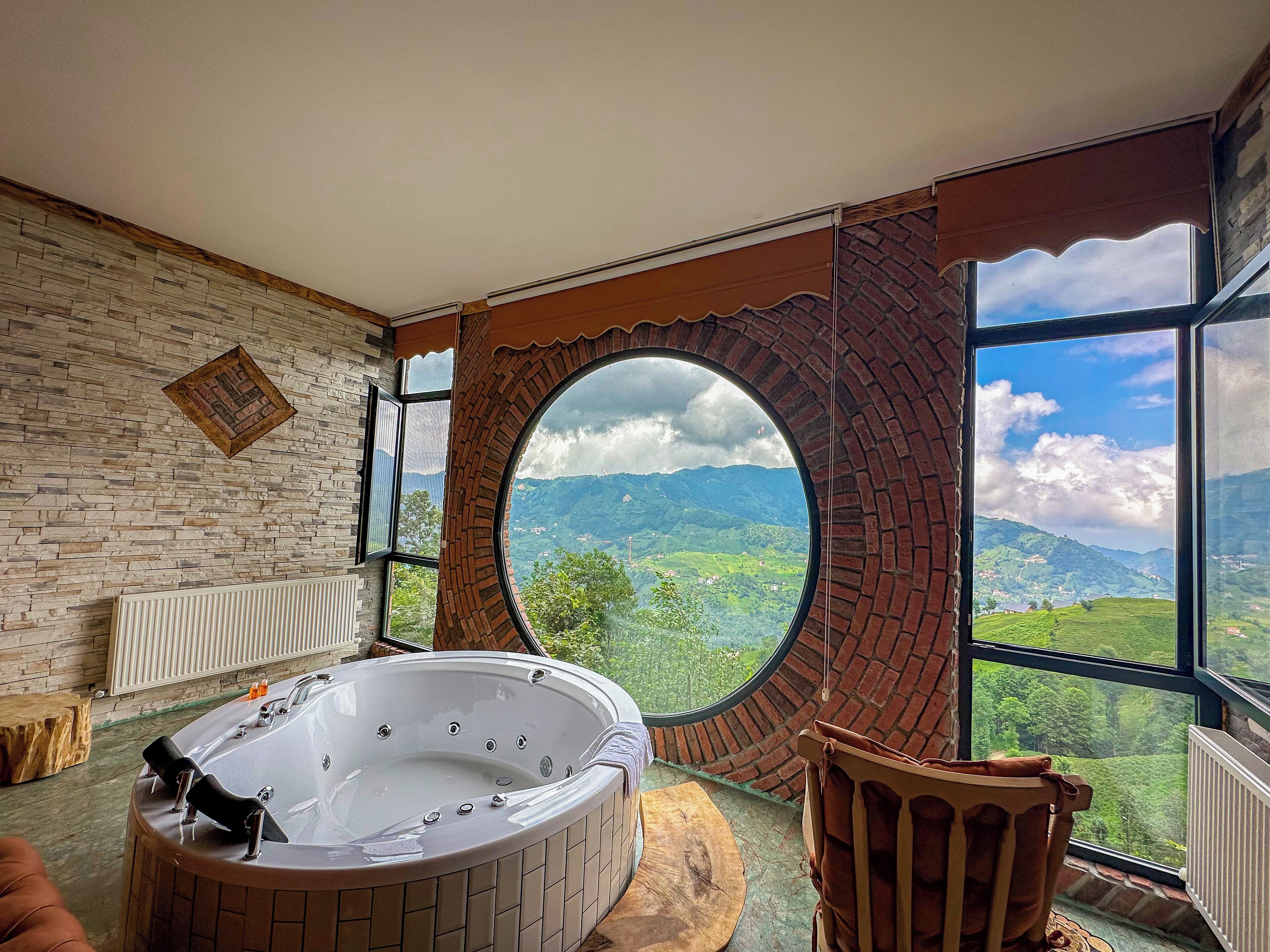 Una habitación con un ventanal circular grande, un jacuzzi y vistas a colinas verdes.