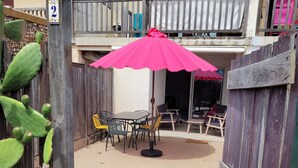 Eine Terrasse mit Tisch und Stühlen, einem rosa Sonnenschirm und einem Holzzaun.