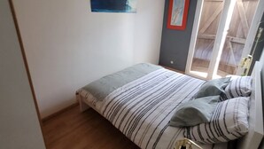 Ein Schlafzimmer mit Bett, Nachttisch mit Lampe, einem Fenster mit Vorhängen und einem Bild an der Wand.