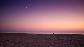 Ein Strand bei Sonnenuntergang, am Himmel ist ein Sichelmond zu sehen.