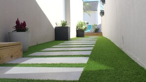 A narrow pathway with artificial grass and concrete slabs, flanked by white walls and potted plants. - So Chic Kerfily, un Petit Coin de Paradis Breton Avec Espace SPA (Locmaria-Plouzané)