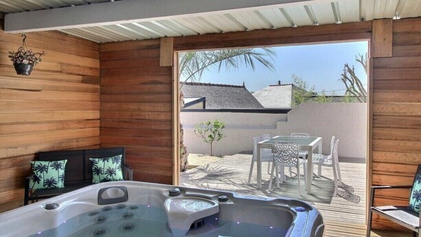 A wooden interior with a hot tub, a small table with chairs, and a view of a patio area with a white fence and palm trees. - So Chic Kerfily, un Petit Coin de Paradis Breton Avec Espace SPA (Locmaria-Plouzané)
