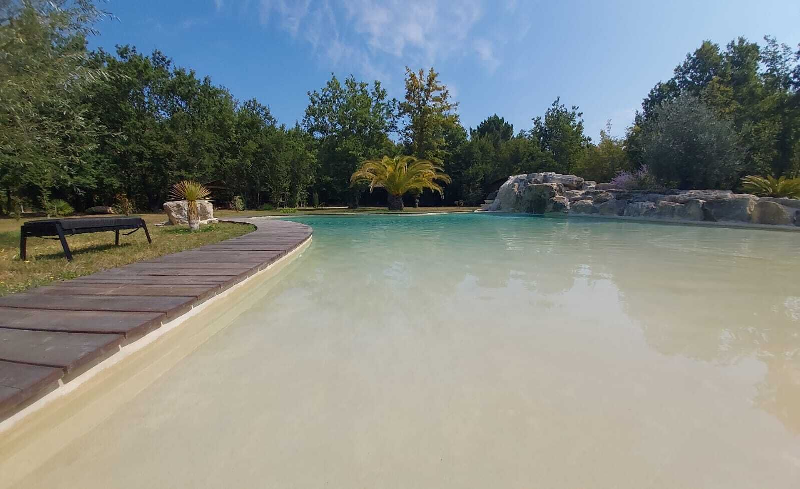 Une piscine aux eaux cristallines, bordée d’une terrasse en bois d’un côté et s’ouvrant sur un paysage rocheux à l’arrière-plan.